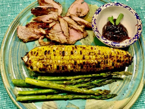 Grilled corn, pork, and asparagus on plate.