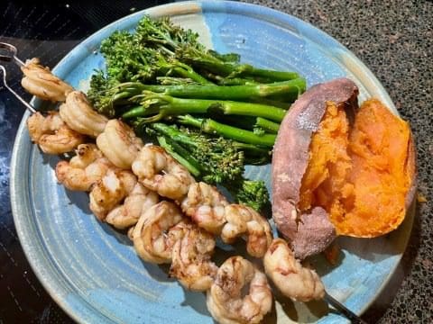 A plate of food with shrimp, broccoli and sweet potato.