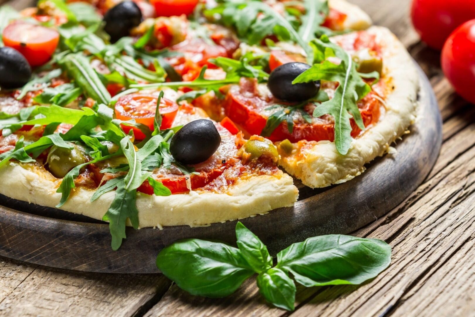 A pizza with olives and basil on top of it.