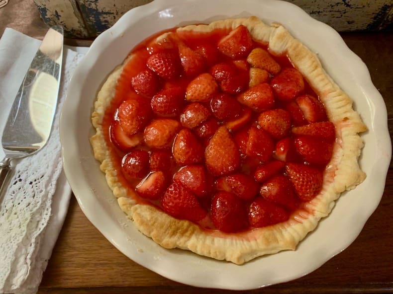 A white plate topped with a strawberry pie.