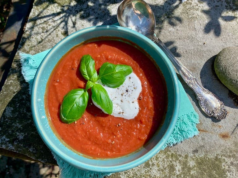 A bowl of tomato soup with basil leaves on top.