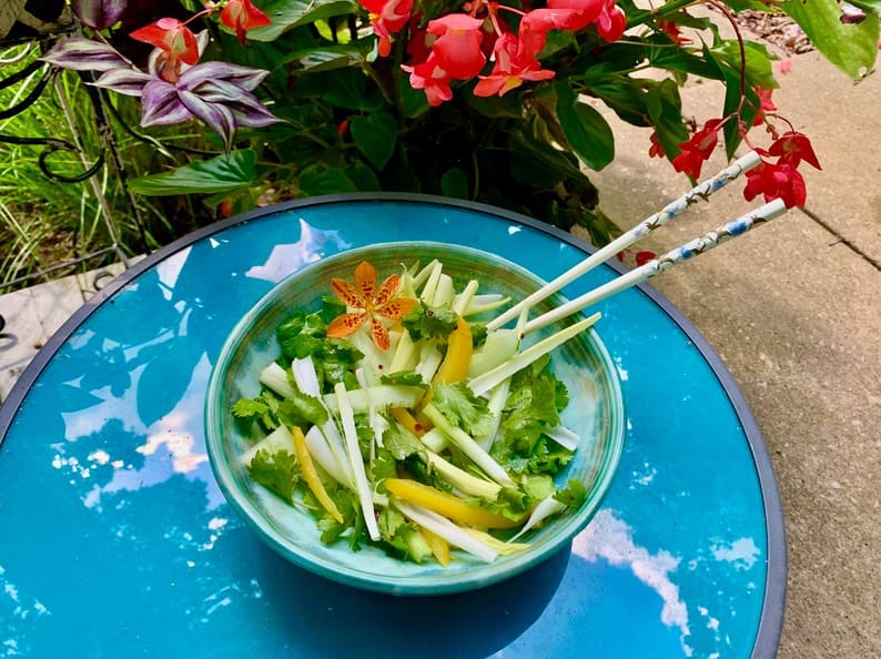 A bowl of salad on the table with chopsticks.