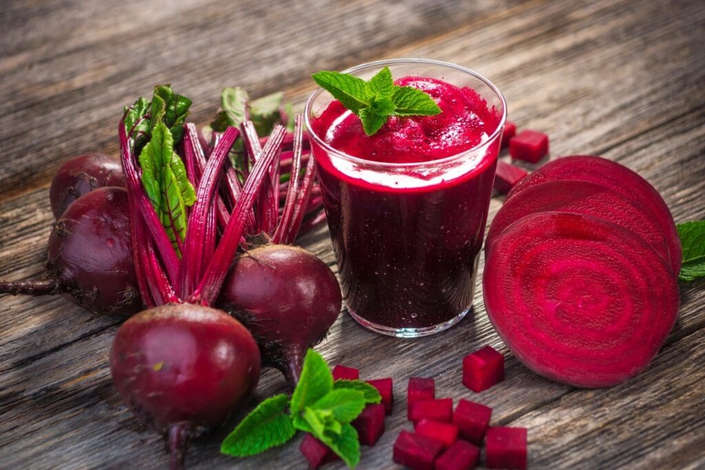 A glass of juice next to some beets and other vegetables.