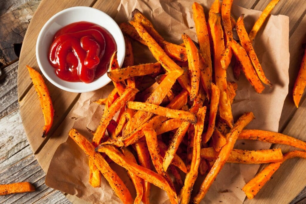 A bowl of ketchup and some fries on paper