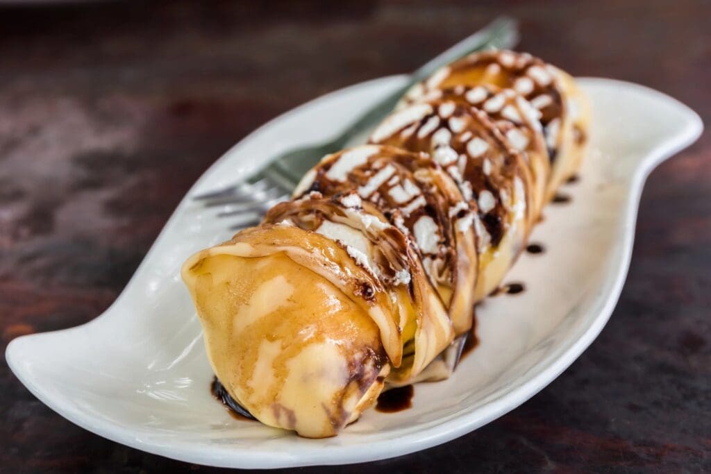 A white plate topped with a crepe covered in chocolate sauce.