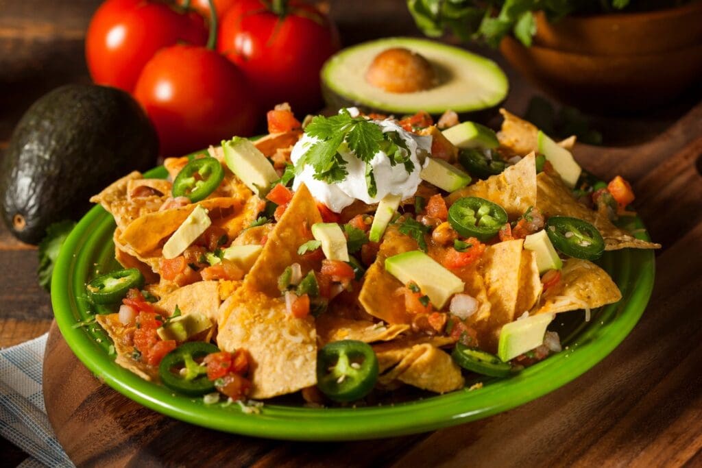 A green plate topped with nachos and avocado.