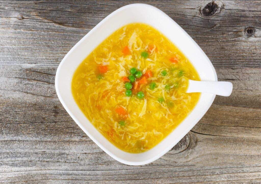 A bowl of soup with carrots and green onions.