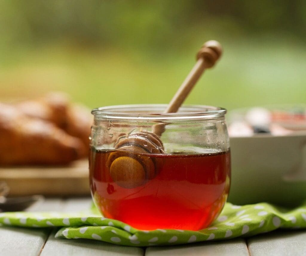 A jar of honey with a wooden stick in it.