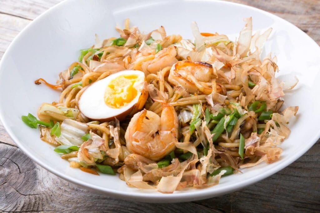 A bowl of food with shrimp and egg on top.