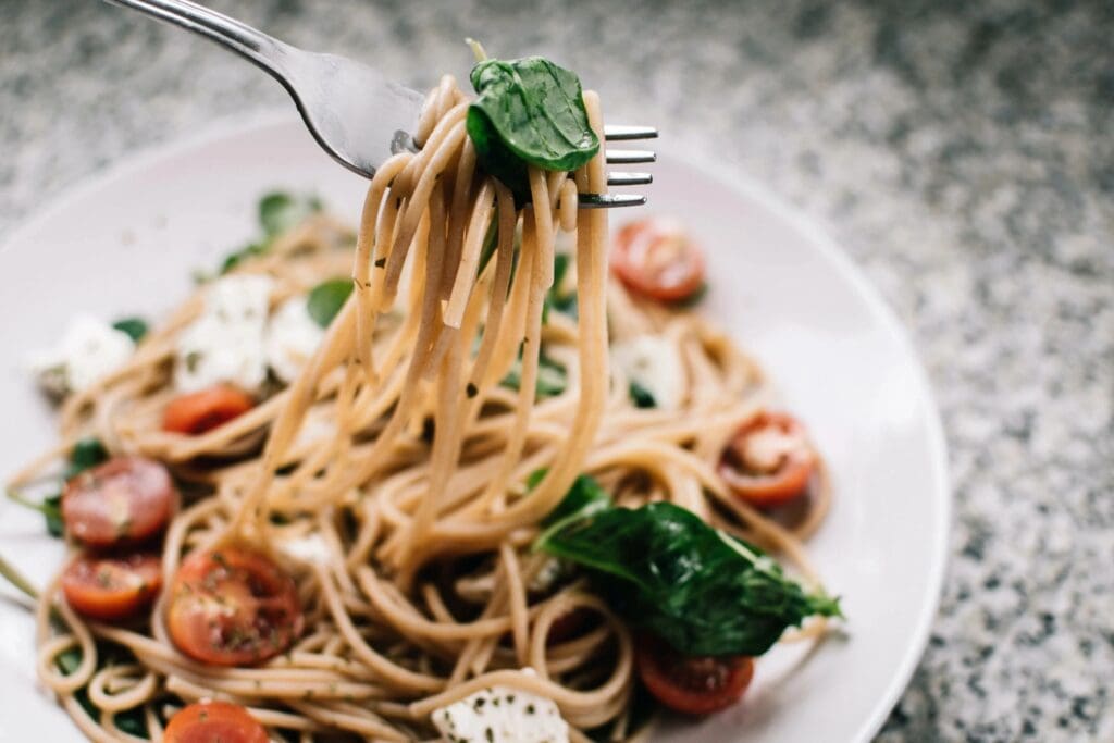 A plate of pasta with spinach and tomatoes.