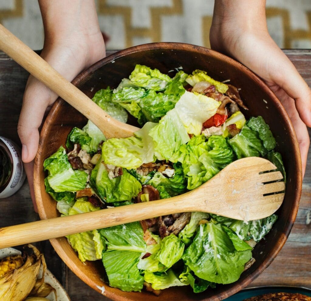 A bowl of salad with wooden utensils in it.