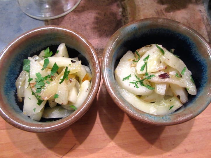 Two bowls of food on a table with wine glasses.