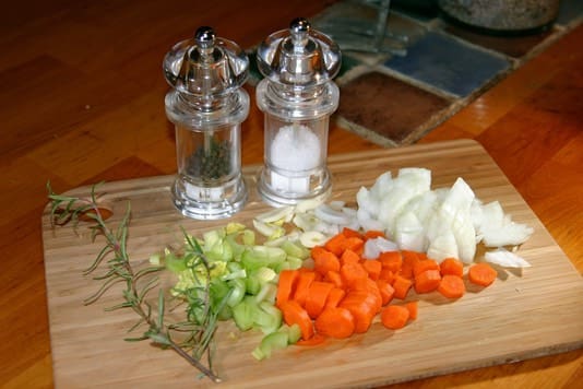 A cutting board with onions, carrots and garlic.