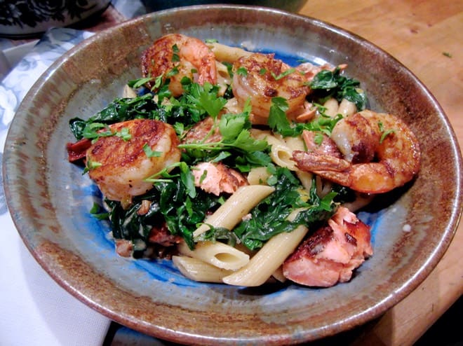 A bowl of pasta with shrimp and greens.