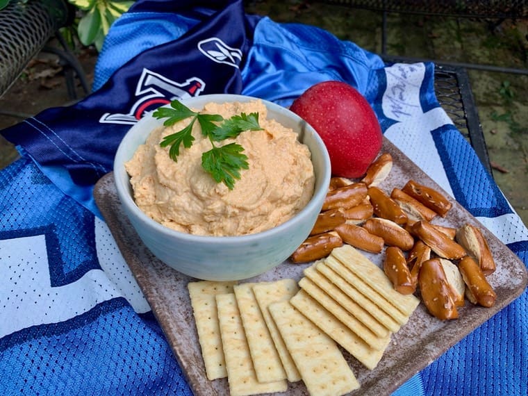 A bowl of dip next to crackers and nuts.