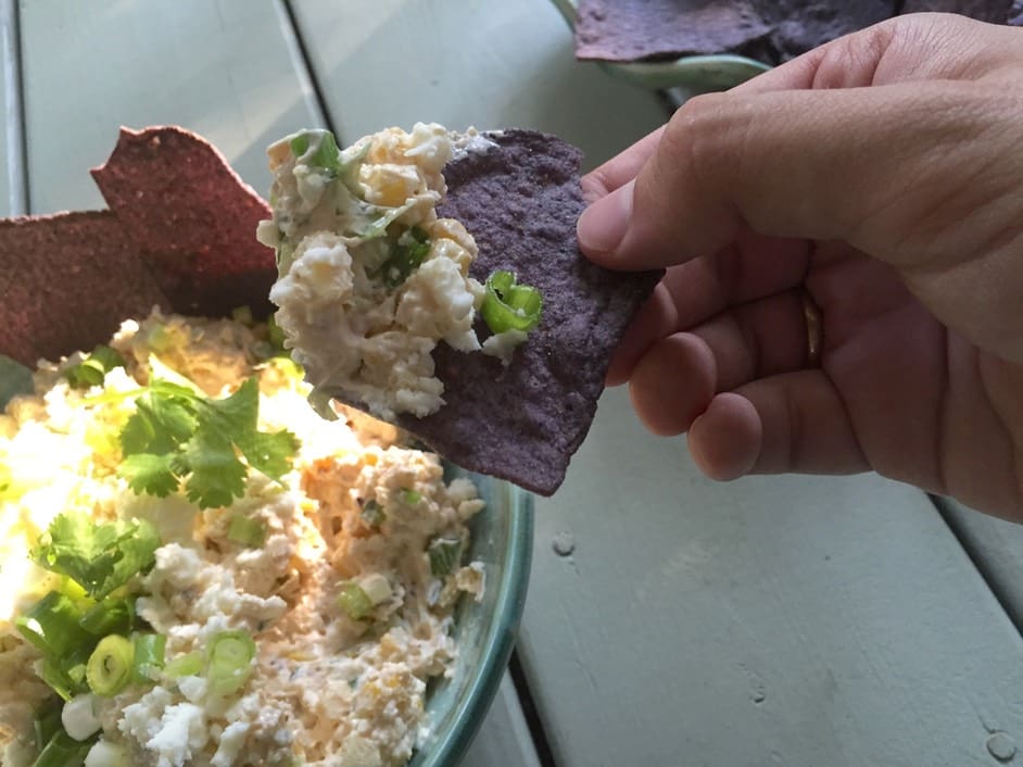 A person holding a tortilla chip over a bowl of rice.