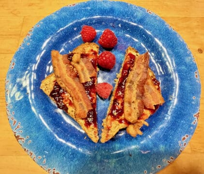 Bacon and raspberry french toast on a blue plate.