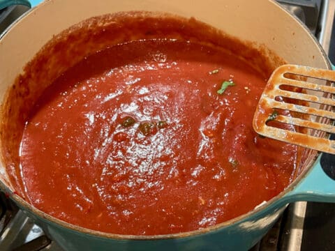 Red sauce simmering in pot with spoon.