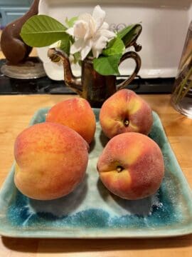 Four ripe peaches on a blue plate.