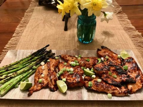 Grilled chicken with asparagus and lime wedges.