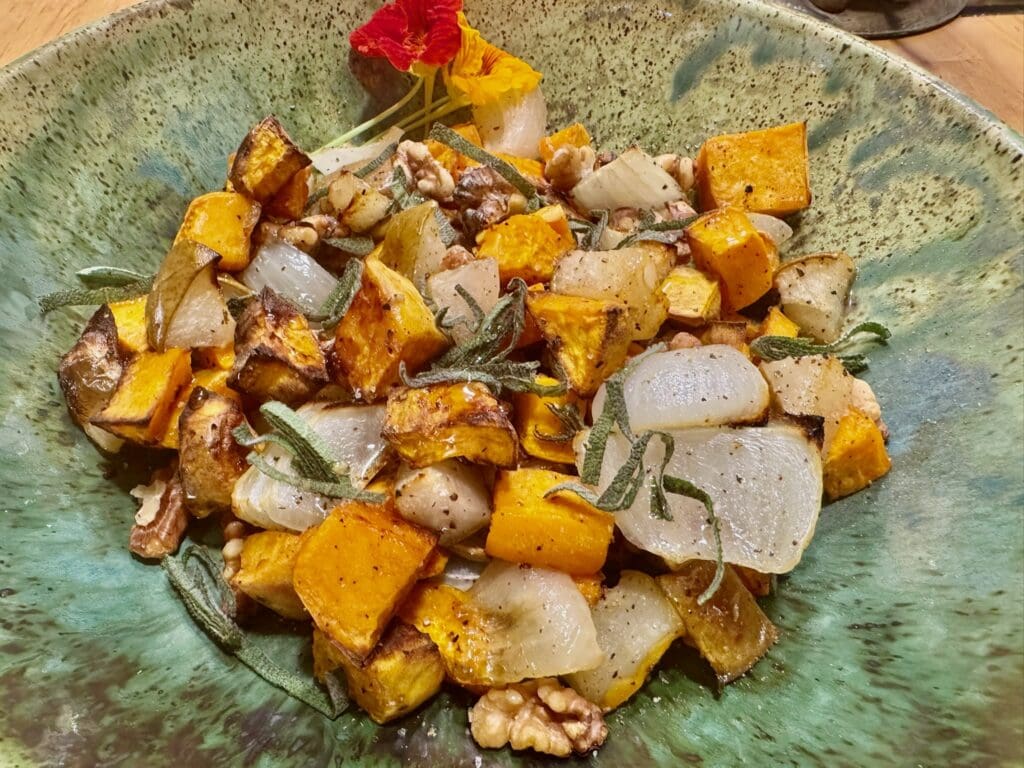 Roasted vegetables with herbs on green plate.