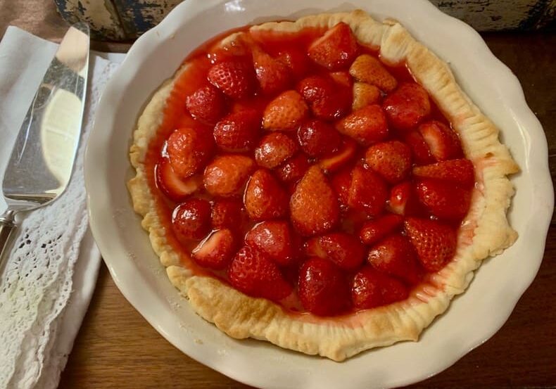 A white plate topped with a strawberry pie.