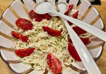 Coleslaw salad with tomato and serving spoons.