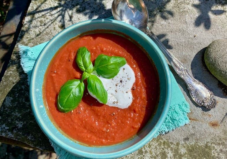 A bowl of tomato soup with basil leaves on top.