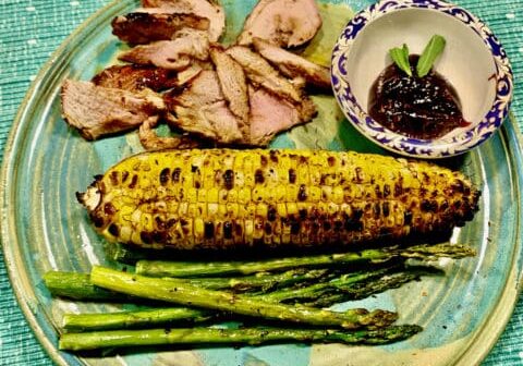 Grilled corn, pork, and asparagus on plate.