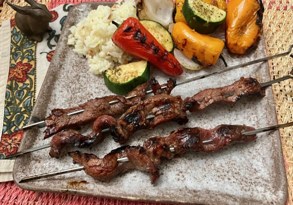 Grilled beef skewers with vegetables and rice.