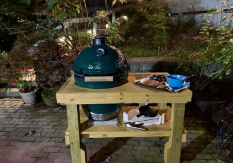 Green egg grill on wooden table outdoors.