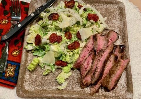 Grilled steak and Caesar salad on a plate.