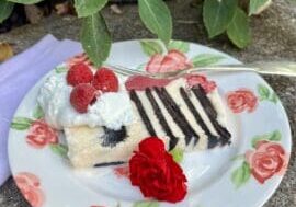 Slice of layered cake with whipped cream and raspberries.