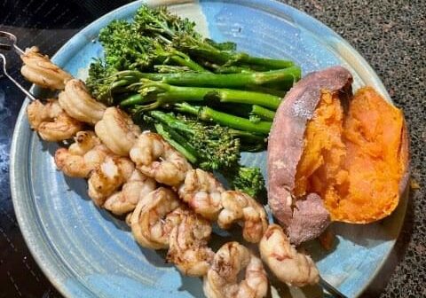 A plate of food with shrimp, broccoli and sweet potato.