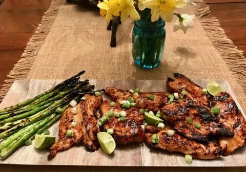 Grilled chicken with asparagus and lime wedges.