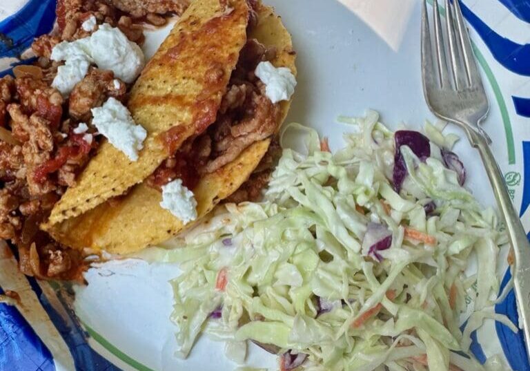 Tacos with coleslaw on a paper plate.