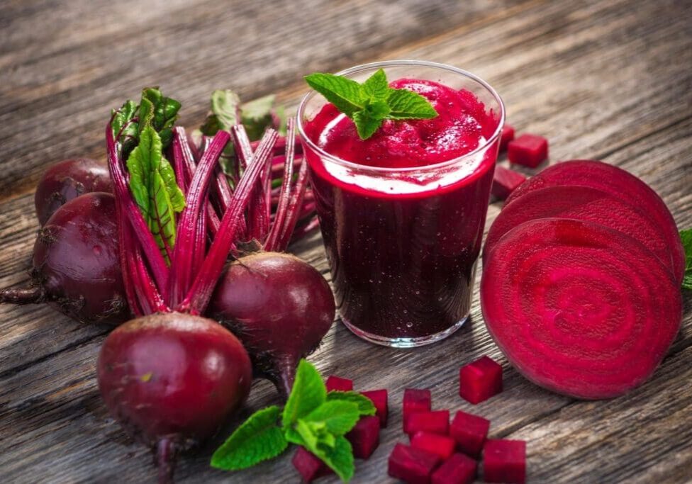 A glass of juice next to some beets and other vegetables.