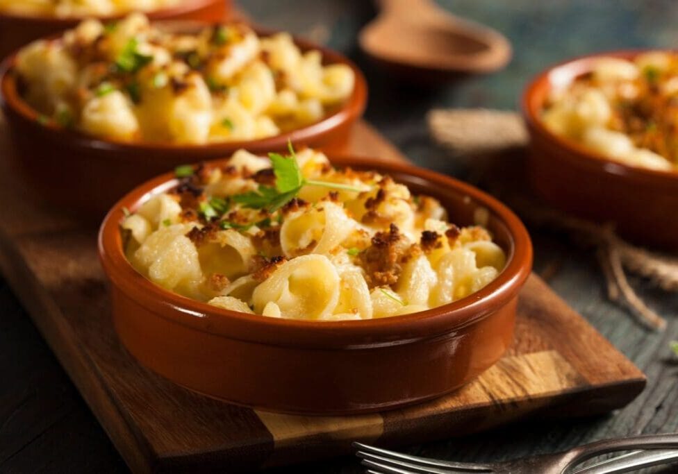 Two bowls of macaroni and cheese on a wooden board.