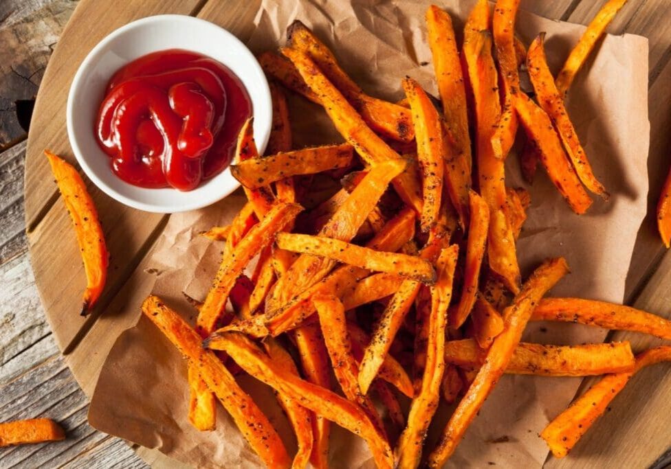 A bowl of ketchup and some fries on paper