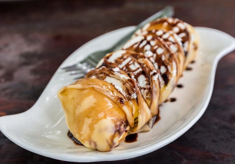 A white plate topped with a crepe covered in chocolate sauce.