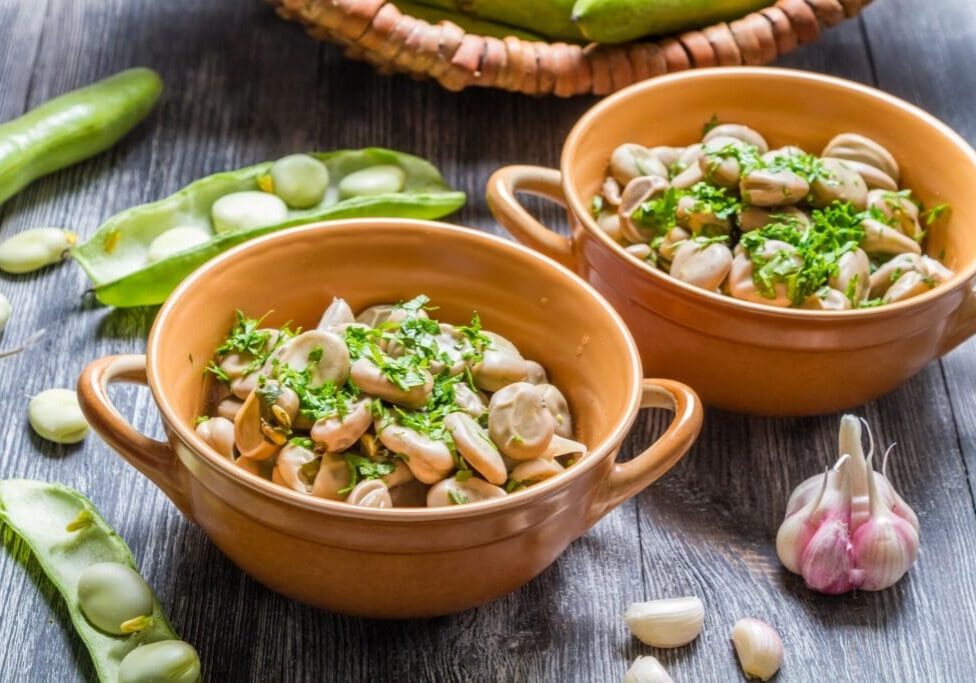 Two bowls of food on a table with green vegetables.