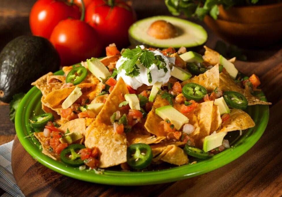 A green plate topped with nachos and avocado.