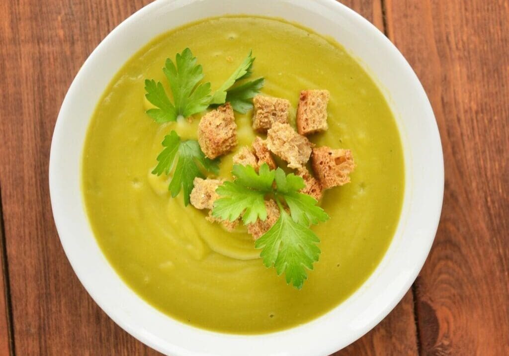 A bowl of soup with croutons and parsley.