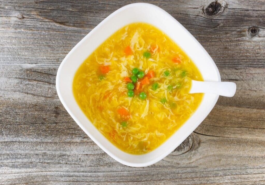 A bowl of soup with carrots and green onions.