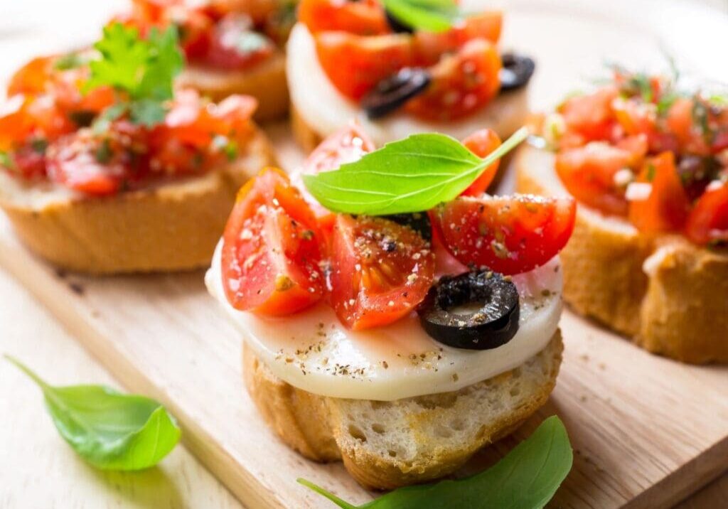 A wooden board topped with slices of bread covered in cheese and tomatoes.