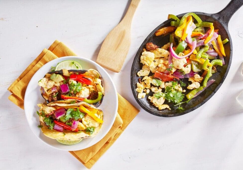 Two bowls of food on a table with a wooden spoon.