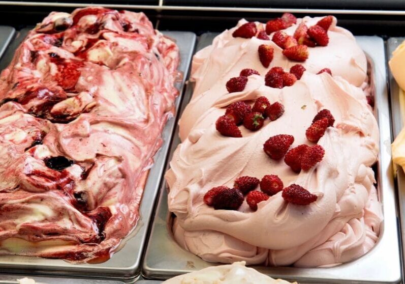 Two pans of strawberry ice cream on a table.