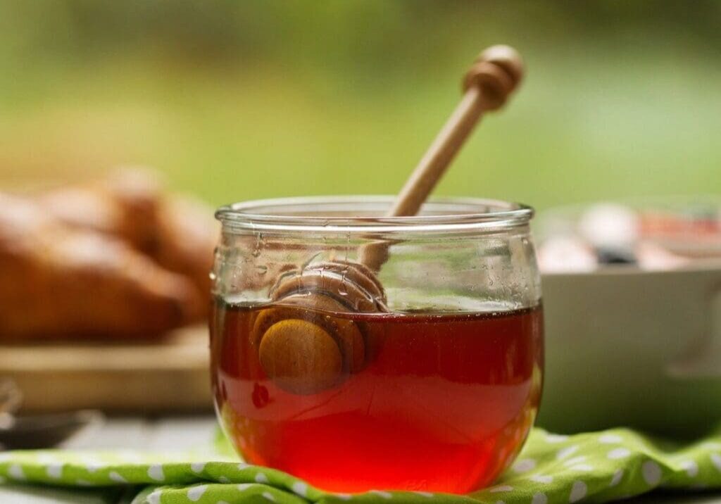 A jar of honey with a wooden stick in it.