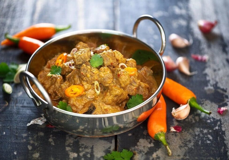 A bowl of stew with carrots and garlic on the side.