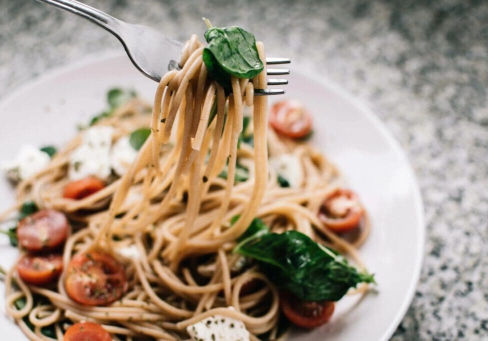 A plate of pasta with spinach and tomatoes.